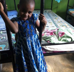 sweetly smiling girl holding onto a bed frame at valentine project children's home-dar es salaam, tanzania