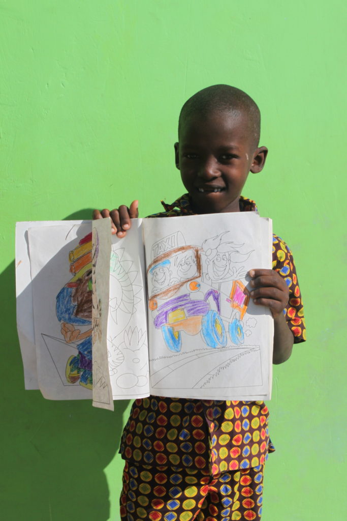 a smiling child holds up his coloring book at the valentine project children's home in dar es salaam tanzania