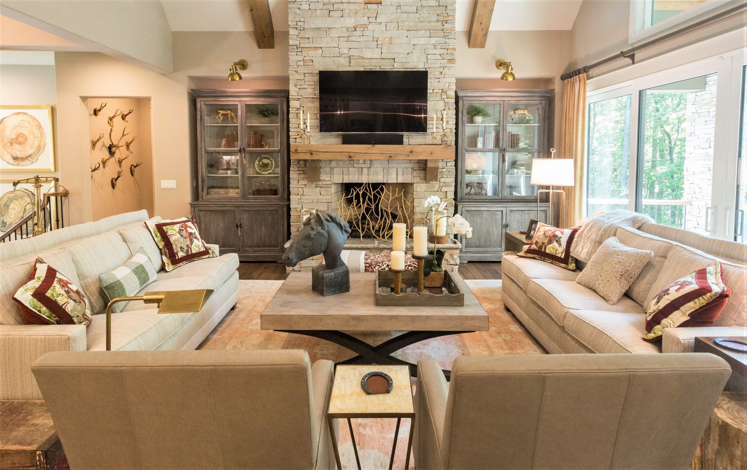 A living room full of warmth and texture found in a Greenville, South Carolina mountain home. Stacked stone fireplace, gold light fixtures, timeless furnishings and rustic cabinetry