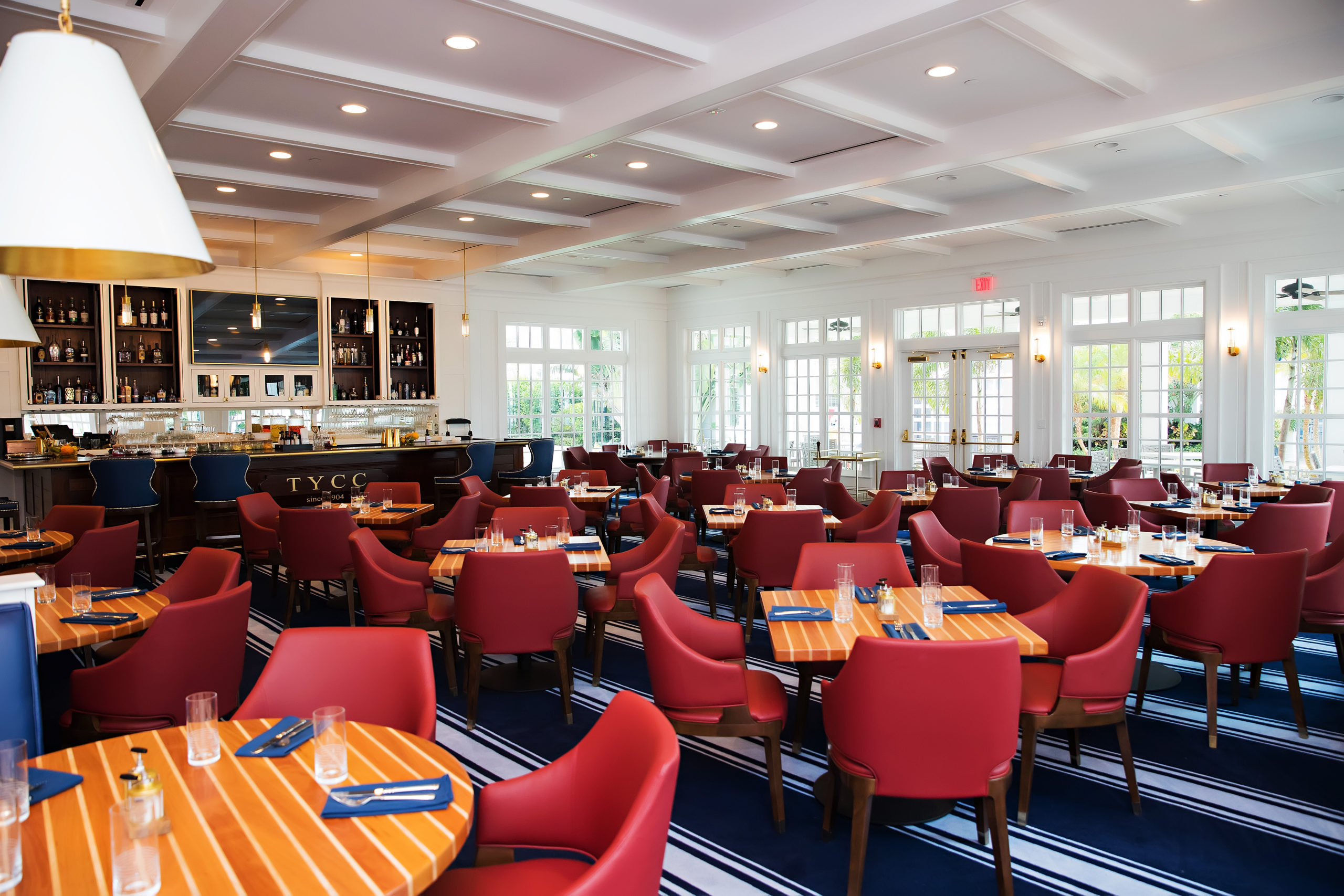 A dining room and bar view at the Tampa Yacht and Country Club with dtriped carpet, red dinign chairs and tables that look like deck.