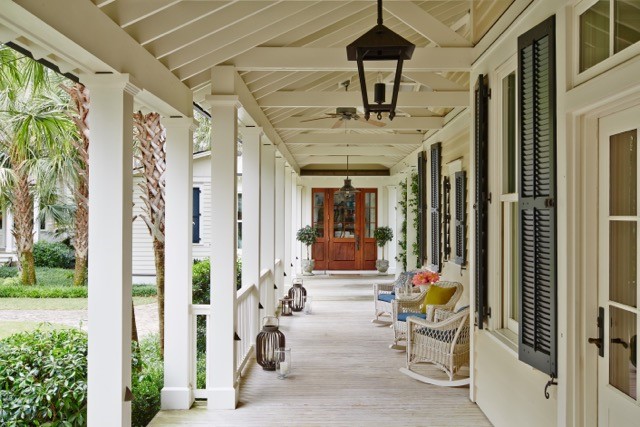 Covered front porch with wicker rocking chairs and lanterns, shutters and a true southern coastal feel is the epitome of lowcountry style designed by J. Banks Design Group